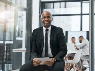 Investing sitting and holding tablet while team of investors works in the background